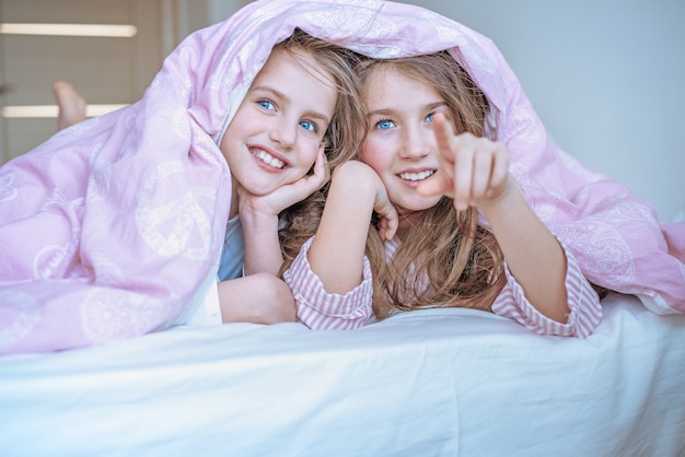 Two little girls in bed are hiding under the covers