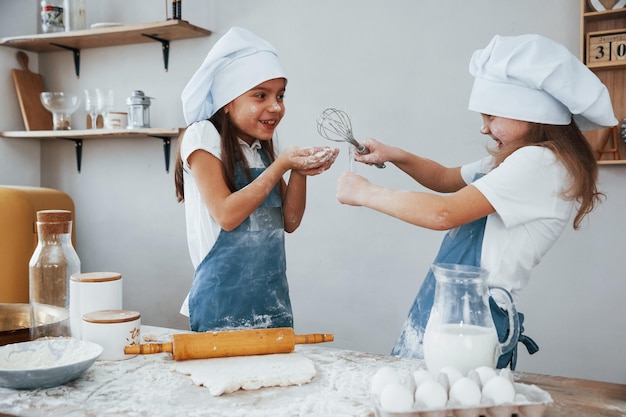 Due bambine in uniforme blu da chef divertendosi e preparando il cibo in cucina