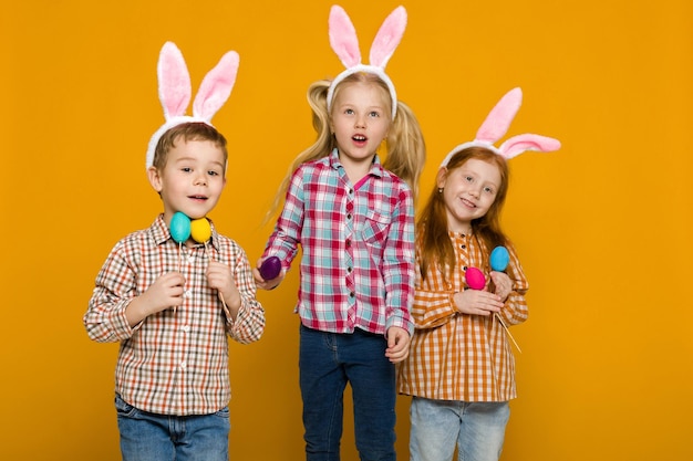 다채로운 계란을 들고 부활절 토끼 귀를 가진 두 어린 소녀와 소년