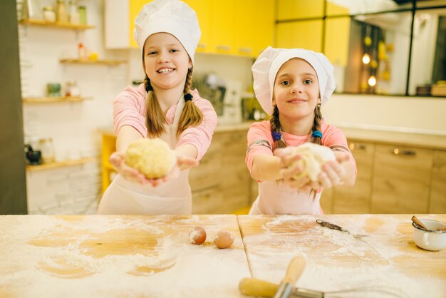 Two little girls cooks in caps shows dough balls