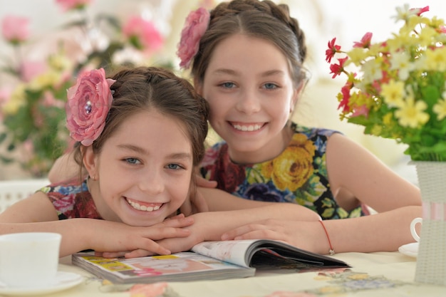 Two little girls in floral dresses reading book and drinking tea