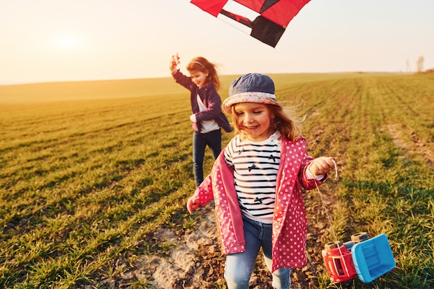 Two little girls friends have fun together with kite and toy car on the field at sunny daytime