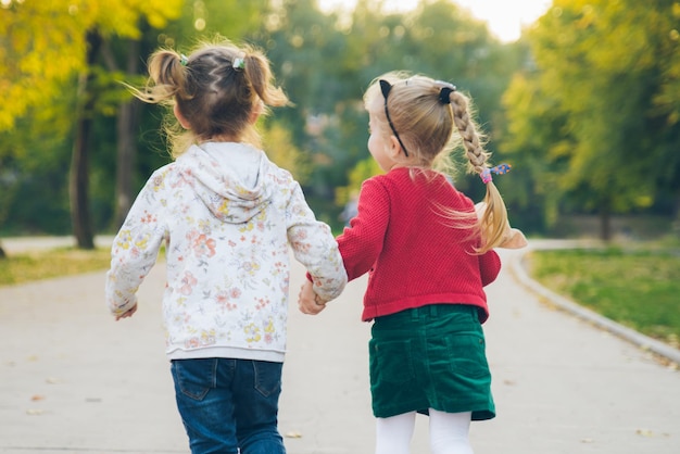 Две маленькие девочки-подружки играют в осеннем городском парке, держась за руки