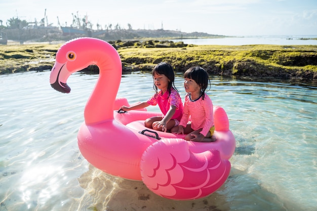 Two little girls happily riding on a flamingo buoy