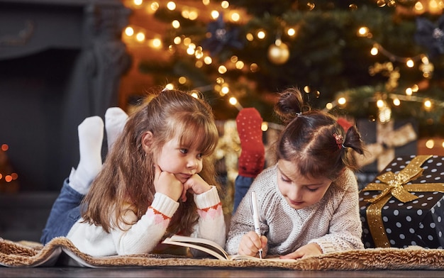 Two little girls have fun in christmas decorated room with gift boxes.