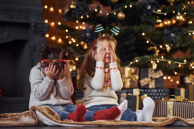 Two little girls have fun in christmas decorated room with gift boxes.