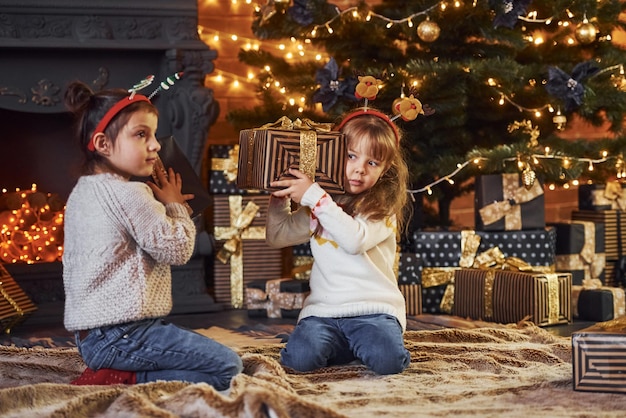 Two little girls have fun in christmas decorated room with gift boxes.