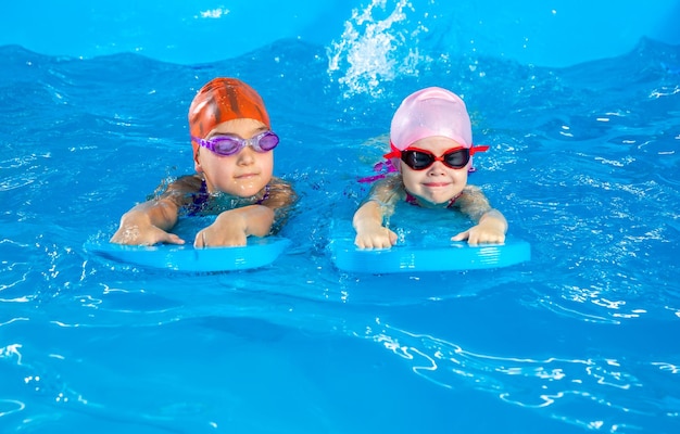 플러터 보드를 사용하여 수영하는 방법을 배우는 수영장에서 즐거운 시간을 보내는 두 어린 소녀