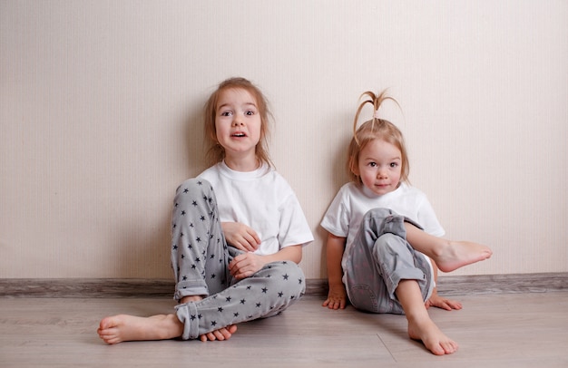 Photo two little girls in home clothes sit at home on the floor near the wall and play merrily with each other. a fun and carefree childhood.