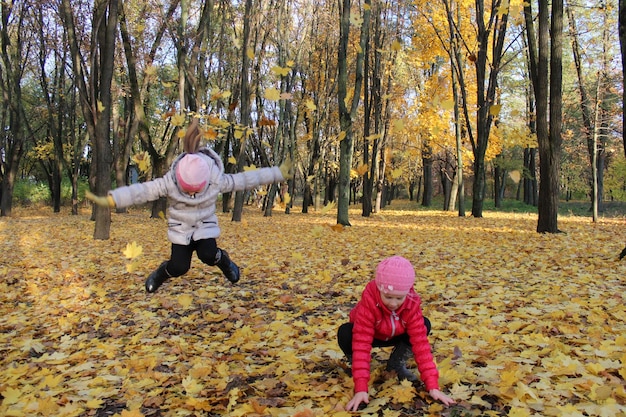 Two little girls jumping in the park with yellow leaves