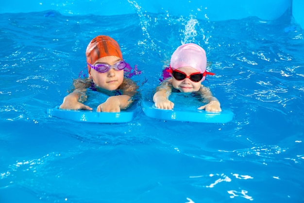 Two little girls learning how to swim in swimming pool using flutter boards