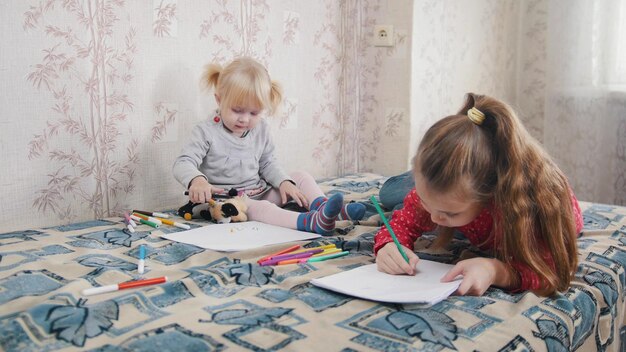 Two little girls lying on the bed and drawing