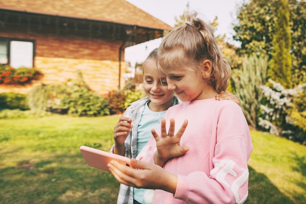 Two little girls outside their house talking on mobile phone with friends