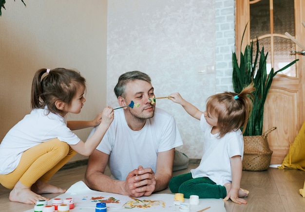 Two little girls paint on dad's face with paint. happy father