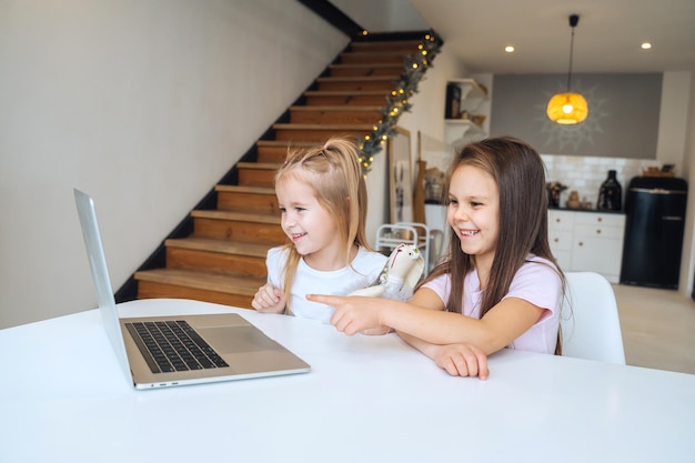 Two little girls playing together at the laptop while sitting at table