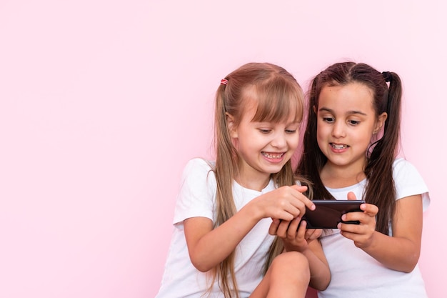 Two little girls playing with smartphones on a pink background