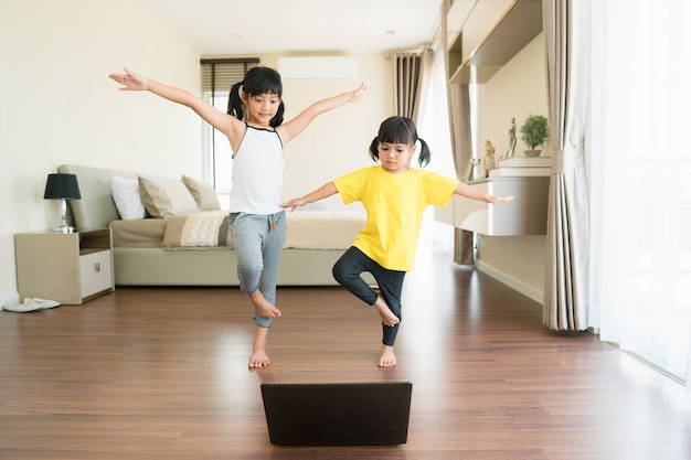 Two little girls practicing yoga, stretching, fitness by video on notebook.