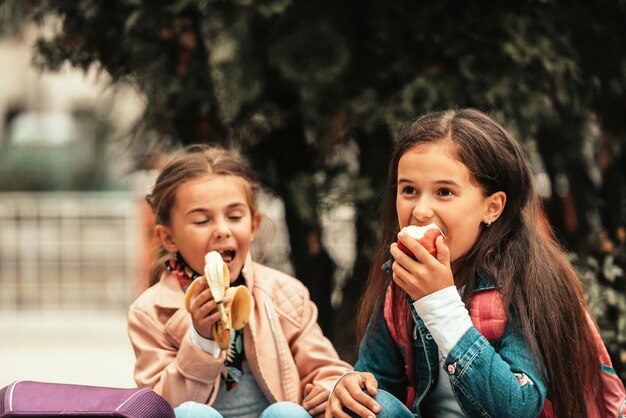 Due bambine durante una pausa pranzo scolastica mangiano banane e mele messa a fuoco selettiva foto di alta qualità