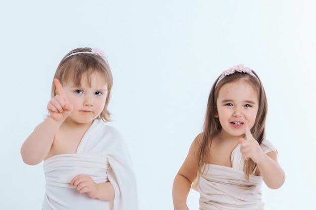 Photo two little girls shake their fingers at a white background. children raise each other. the concept of education , childhood, and sisterhood. copy space