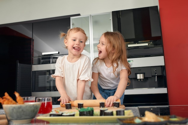 Two little girls siblings having fun and eating on the kitchen at home with japanese food