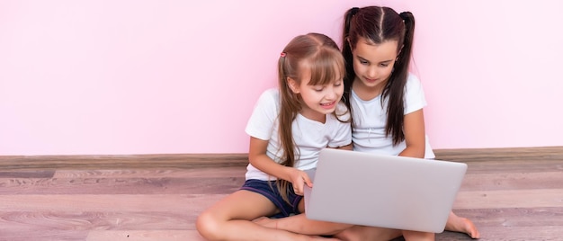 Due bambine sedute davanti a un laptop e ridono, primo piano, emozioni positive, intrattenimento su internet per bambini