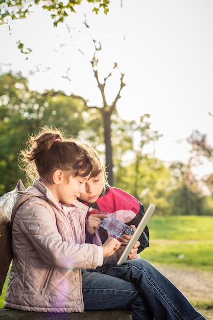 two little girls using tablet on the bench