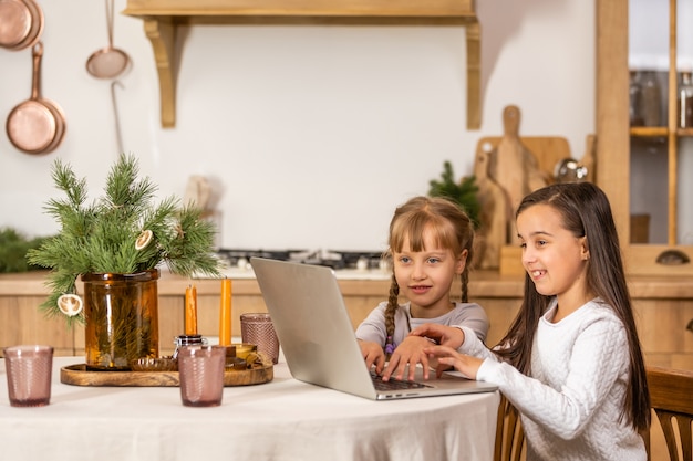 Two little girls watching online school while sitting at table dining room table.