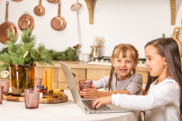 テーブルダイニングルームのテーブルに座ってオンライン学校を見ている2人の少女。