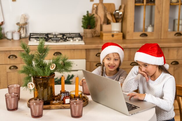 Две маленькие девочки смотрят онлайн-школу, сидя за столом в обеденном зале.