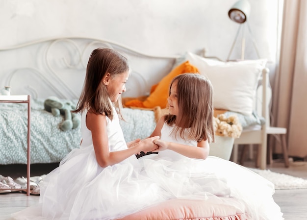 Two little girls in white dresses in a bright studio have joj