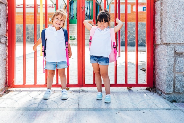 Two little girls with backpacks at the school entrance door