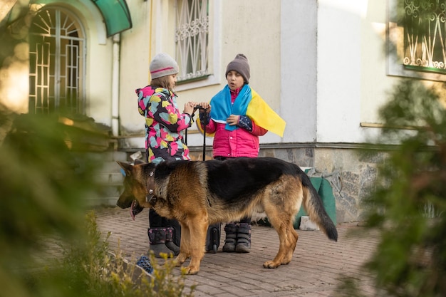 ウクライナ、スーツケース、犬の旗を持つ2人の少女。ウクライナ戦争の移住。スーツケースの中のもののコレクション。ウクライナの旗、助けて。クリジン、軍事紛争。