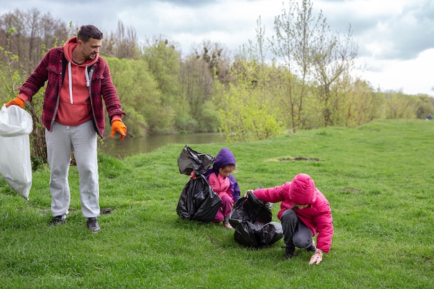 Two little girls with their dad, with garbage bags on a trip to nature, are cleaning the environment.