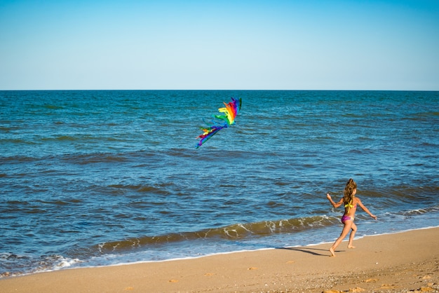 Two little happy cheerful girls run with a kite on the sandy shore by the sea