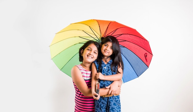 白で隔離、カラフルな傘を持つ2つの小さなインドの女の子
