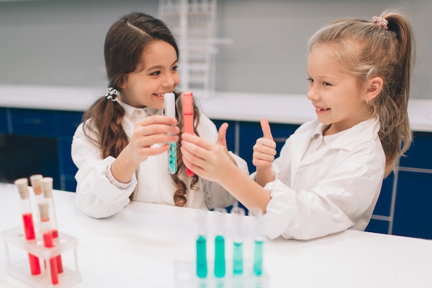 Two little kids in lab coat learning chemistry in school laboratory. Young scientists in protective glasses making experiment in lab or chemical cabinet. Studying ingredients for experiments .