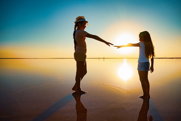 Two little lovely happy sisters are walking along the mirror-like pink salt lake enjoying the warm summer sun in the long-awaited vacation