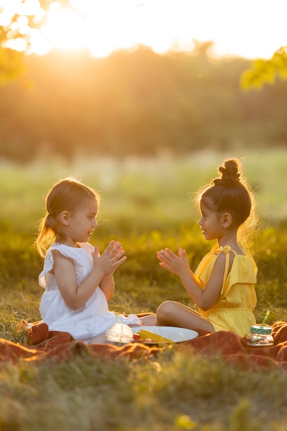 Two little mixed race girls play talk and share secrets in the park outdoors sitting on a blanket