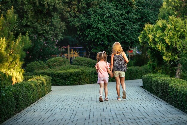 晴れた日に遊園地で手をつないで歩く、年齢の異なる2人の妹の女の子