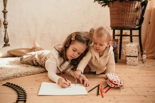 Two little sisters are lying on the floor and drawing on paper