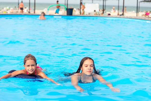 Две маленькие сестренки плавают в большом бассейне на пляже