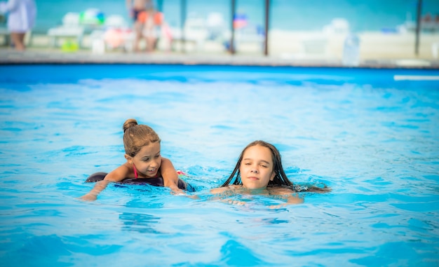 Two little sisters girls are swimming in a large pool in the beach