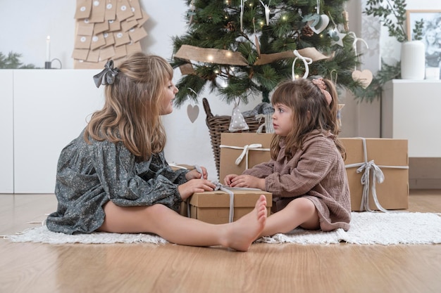 Two little sisters opening a gift near the christmas tree at home