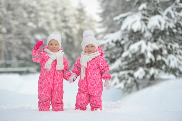 Two little twin girls in red suits stand in a snowy winter forest.