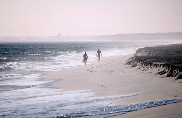 Due figure solitarie che camminano fianco a fianco sul litorale della spiaggia in una giornata ventosa.