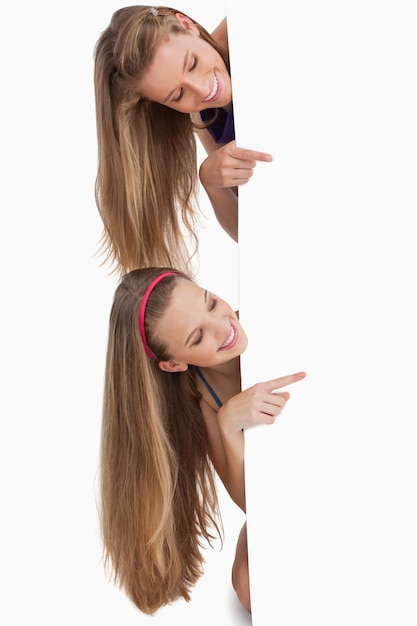 Two long hair students pointing behind a blank sign