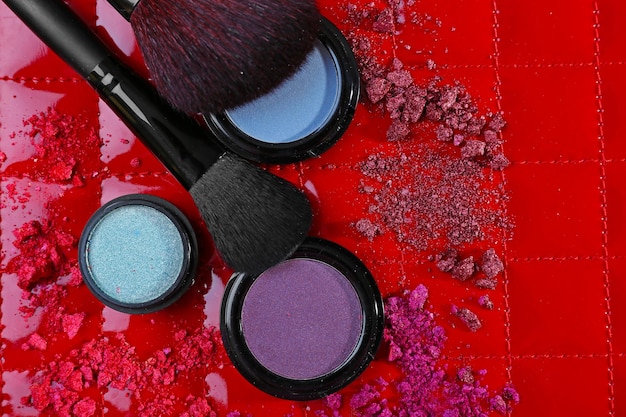 Two makeup brushes with shadows and pink rouges on red background closeup