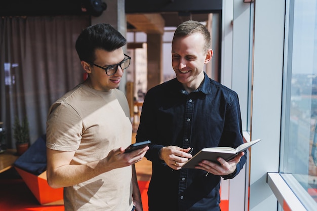 Two male businessman managers stand near the window in a modern office and discuss a new project Two men with glasses are talking about a new business