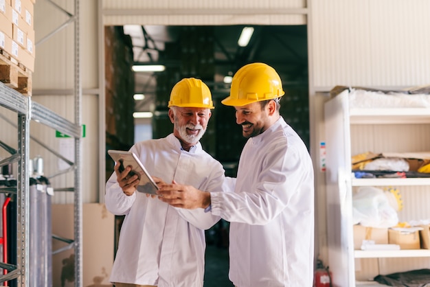 Two male colleagues looking at tablet while standing in warehouse.