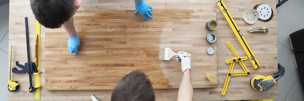 Two male construction workers are covering wood floor with protective layer of varnish